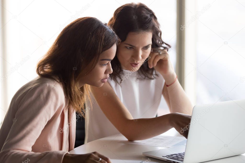 Serious diverse women working on laptop discussing project