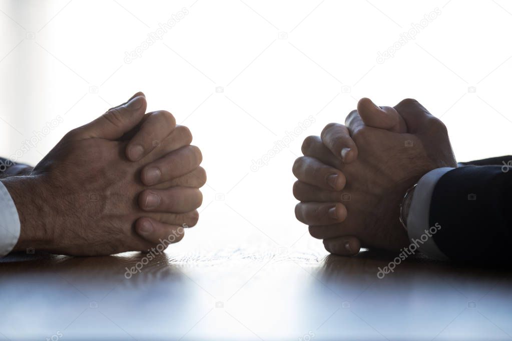Close up of businessmen sit at table with hands clenched