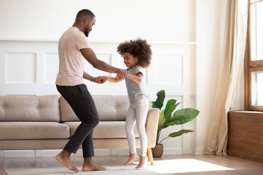 Happy african father and kid daughter jump dance at home