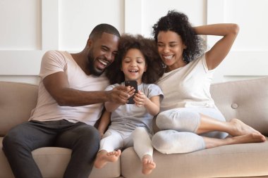 Afrika kızı ve ebeveyn akıllı telefona bakarak kanepede gülüyor