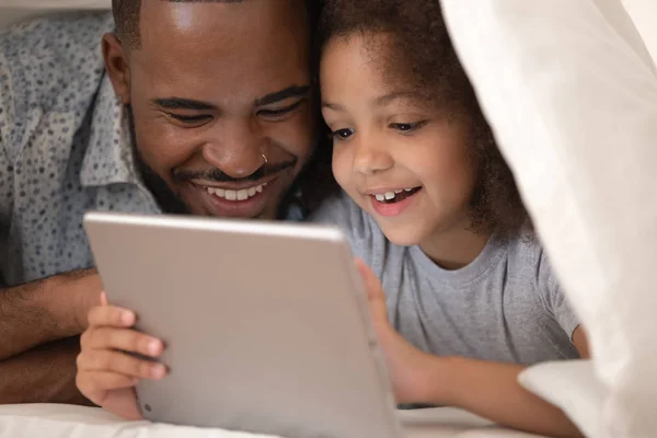 Africano pai e filha usando tablet na cama sob cobertor — Fotografia de Stock