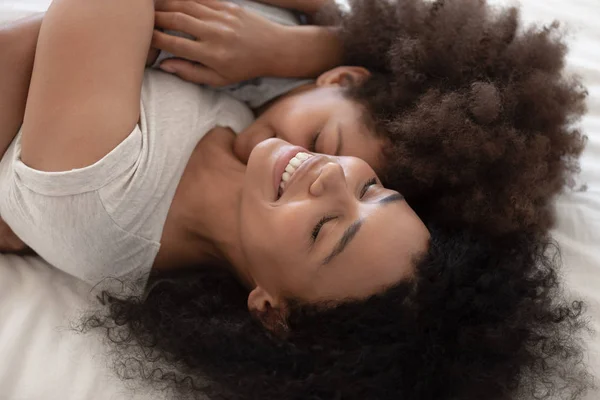 Afectuosa africana mamá y niño hija abrazando acostado en la cama — Foto de Stock