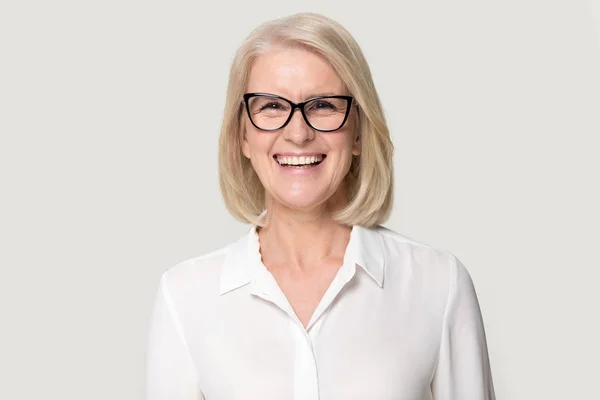 Смеющаяся взрослая деловая женщина в очках, позирующая на фоне серой студии — стоковое фото