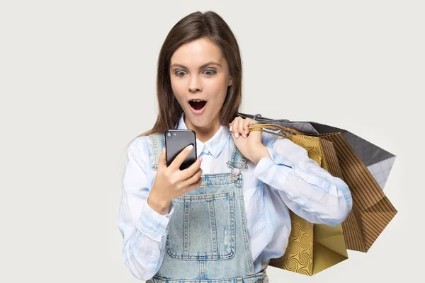 Förvånad kvinna Shopper hålla shopping väskor tittar på smartphone skärmen — Stockfoto