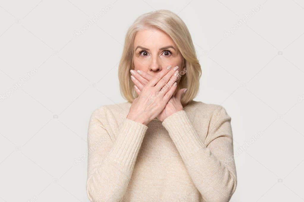 Shocked aged female covering mouth with hands feel scared