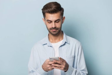Ciddi adam mavi stüdyo arka planda izole Smartphone ayakta tutarak