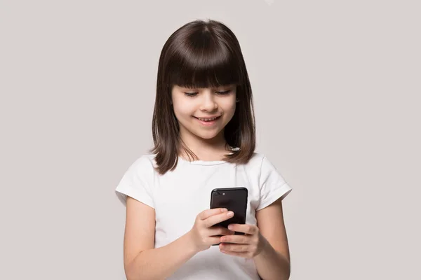 Little girl using smart phone posing isolated on grey background — Stock Photo, Image