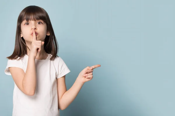 Lustiges kleines Mädchen hält Finger auf Lippen, die auf Copyspace zeigen — Stockfoto