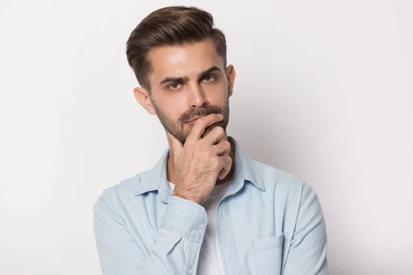 Thoughtful young man holding hand on chin feeling doubtful — Stock Photo, Image