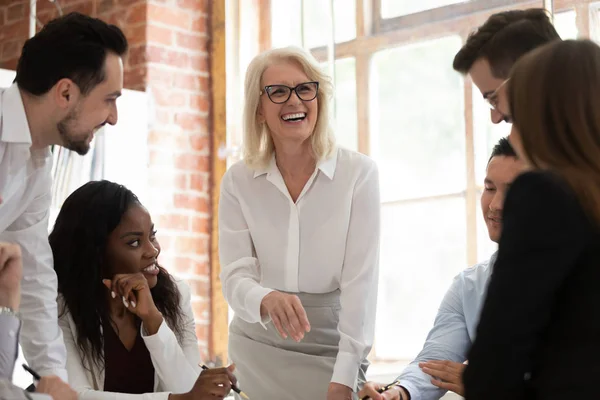 Vrolijke multiculturele jonge medewerkers met oude mentor lachend samenwerken — Stockfoto