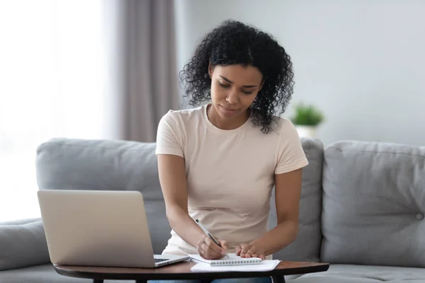 Enfocado chica africana estudiante estudio en línea en casa haciendo notas —  Fotos de Stock