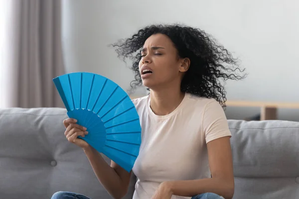 Surriscaldato africano giovane donna sentirsi caldo agitando ventilatore a casa — Foto Stock