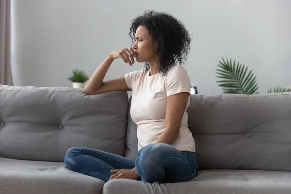 Triste riflessivo africano ragazza su divano guardando lontano sentire depresso — Foto Stock