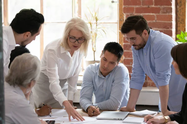 Serious old woman leader coach teach young workers explain paperwork