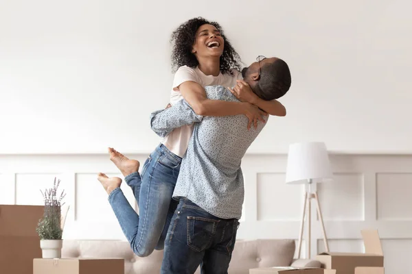 African husband lifting happy wife celebrating moving day with boxes — Stock Photo, Image
