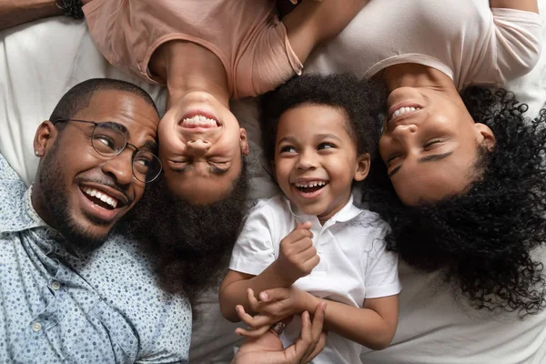 Funny affectionate african parents and kids laughing lying on bed — Stock Photo, Image