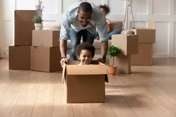 Happy african dad playing with little son riding in box — Stock Photo, Image