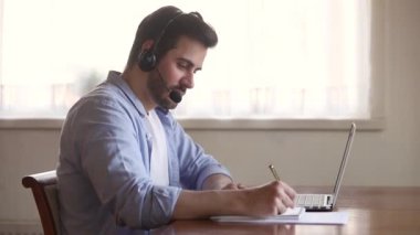 Kulaklık takan Skype öğretmeni dizüstü bilgisayar ekranına bakarak notlar hazırlıyor