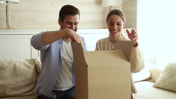 Feliz pareja emocionada clientes abrir caja de cartón sentado en el sofá — Vídeo de stock