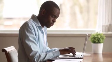 Dizüstü bilgisayar belgeleri ile çalışan odaklanmış siyah adam masada oturup