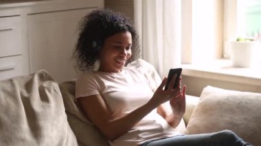 Mutlu genç Afrikalı kadın akıllı telefon kullanarak kablosuz kulaklık giyiyor
