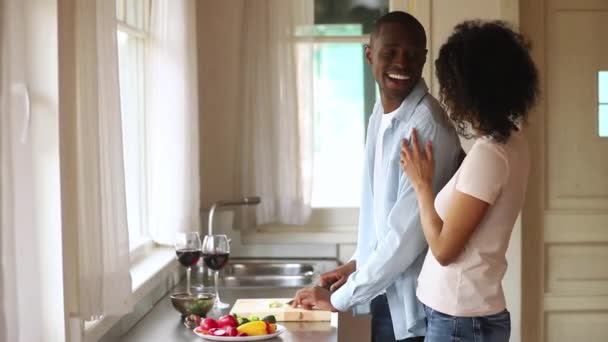 Счастливая африканская жена обнимает мужа, готовящего здоровую еду за ужином — стоковое видео