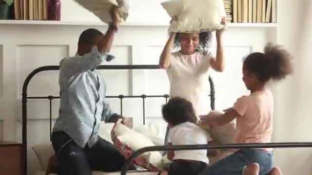 Heureuse famille africaine et les enfants ayant une bataille d'oreillers sur le lit — Video