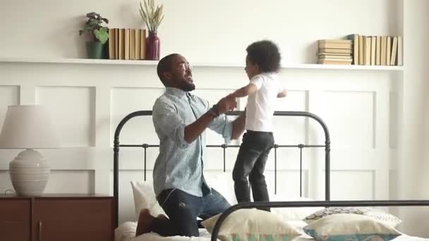 Счастливый африканский отец играет с ребенком сын прыгает на кровать — стоковое видео