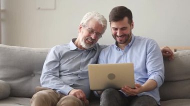 Mutlu yaşlı baba ve genç oğlu evde dizüstü bilgisayar kullanarak