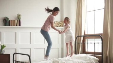 Mutlu anne ve küçük kızı yatakta atlayarak el ele tutuşuyor