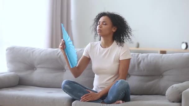 Africano mulher acenando fã sentindo quente sofrimento de calor dentro de casa — Vídeo de Stock