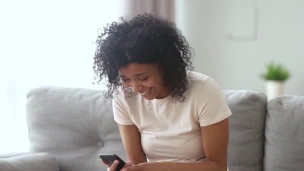 Ευτυχισμένη αφρικανική γυναίκα κοιτάζοντας το τηλέφωνο γελώντας με αστείο αστείο — Αρχείο Βίντεο
