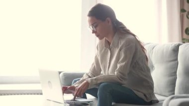 Dizüstü bilgisayarda yazarak evden çalışan odaklanmış genç kadın freelancer