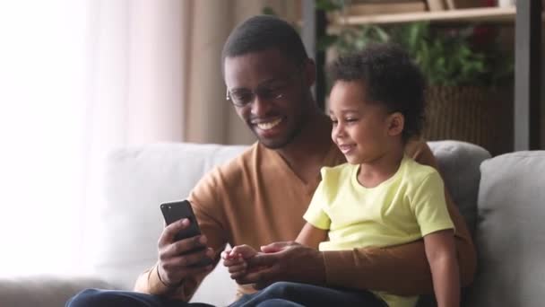 Щасливий африканський тато і маленький син сміється дивлячись на телефон — стокове відео