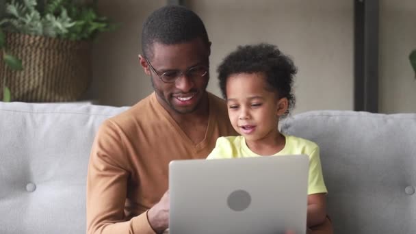 Šťastný černý otec učí chlapečku, aby četl použití přenosného počítače — Stock video