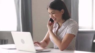 Asyalı iş kadını ofiste telefonda konuşurken dizüstü bilgisayar kullanarak