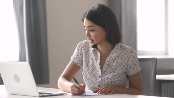 Asiática empresária vestindo fone de ouvido fazer anotações falar por teleconferência — Vídeo de Stock