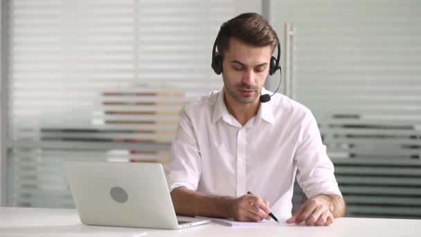 Biznesmen nosić słuchawki rozmowa z klientem na laptop pisać notatki — Wideo stockowe