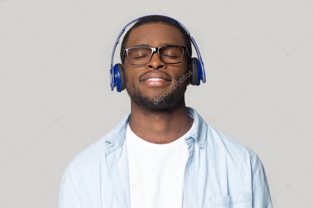 Smiling black man in glasses enjoy music in Bluetooth headphones