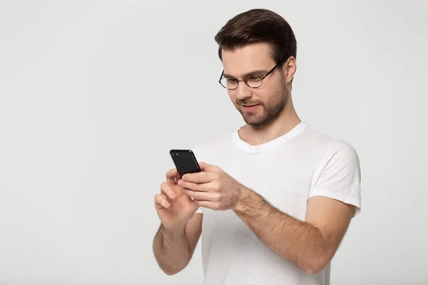 안경을 쓰고 있는 남자가 휴대 전화를 사용하여 회색 배경에 포즈를 취합니다. — 스톡 사진