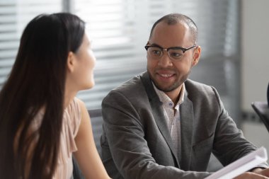 Gülümseyen Afrikalı işadamı ofiste Asyalı kadın meslektaşı ile konuşuyor