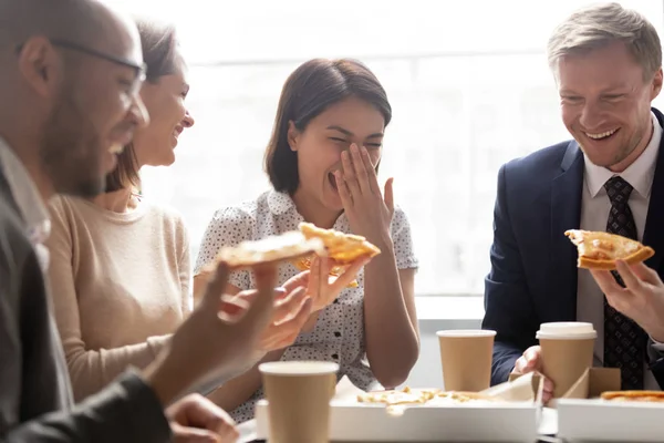 Счастливый азиатский рабочий смеется держать ломтик едят пиццу с коллегами — стоковое фото