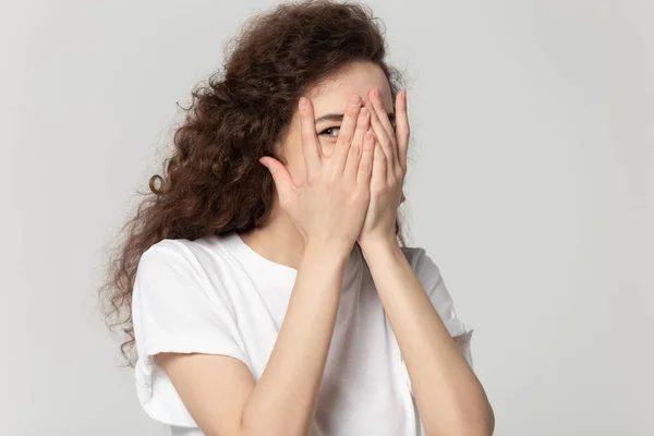 Sly girl hiding face behind hands peeps through fingers — Stock Photo, Image