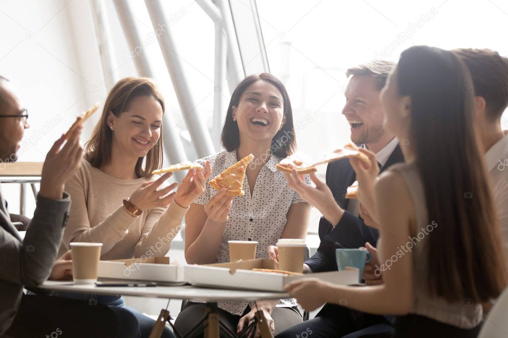 Cheerful multicultural team workers laugh share lunch meal eating pizza