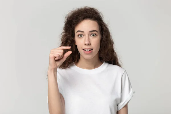 Woman look at camera showing with fingers something small — Stock Photo, Image