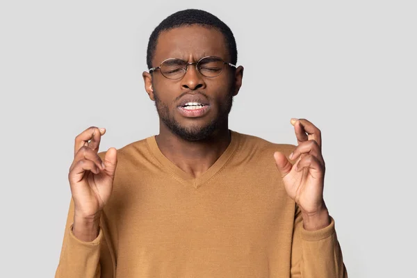 Esperanzado hombre negro en gafas cruzan los dedos pidiendo deseo —  Fotos de Stock