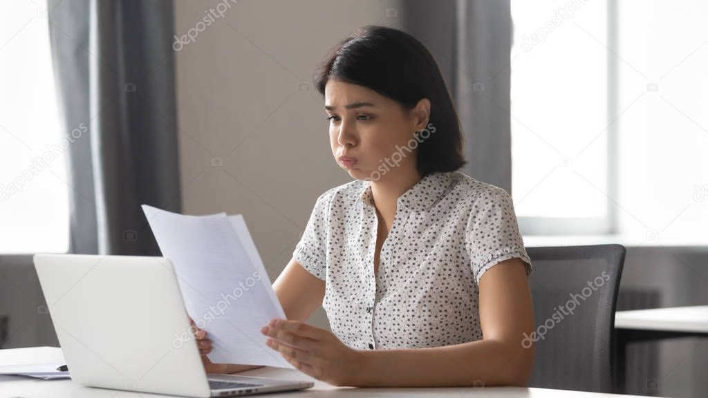 Stressed upset asian business woman reading bad news in paper