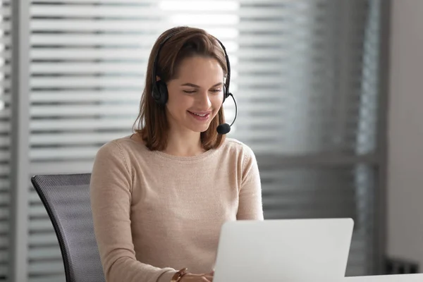 Smiling businesswoman receptionist wear wireless headset video calling on computer — Stock Photo, Image