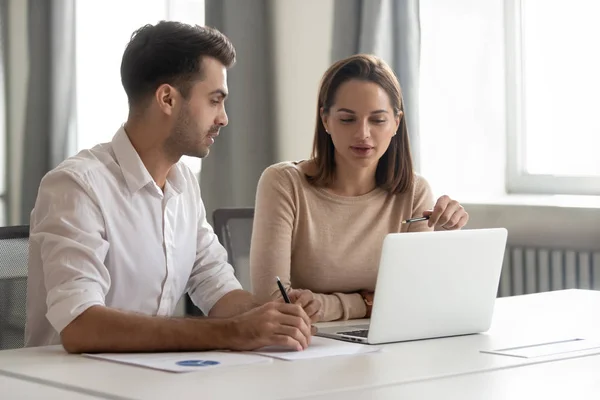 Female mentor talking teaching male colleague intern looking at laptop — Stock Photo, Image