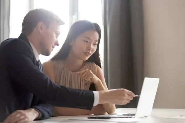 Útil masculino caucasiano mentor instruindo asiático estagiário apontando para laptop — Fotografia de Stock